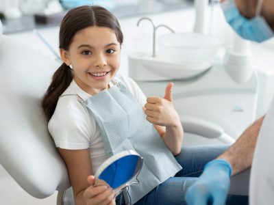 portrait of girl sitting in dental chair, showing thumb up and smiling at the camera